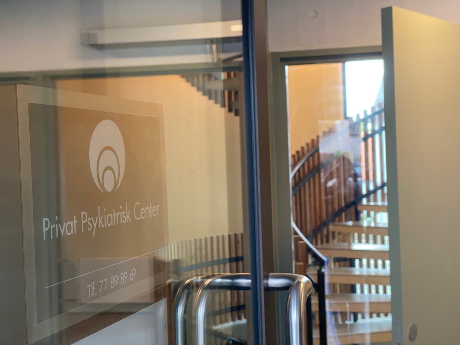 Indgangsdøren til Privat Psykiatrisk Center Aalborg med logo og telefonnummer på glasdøren