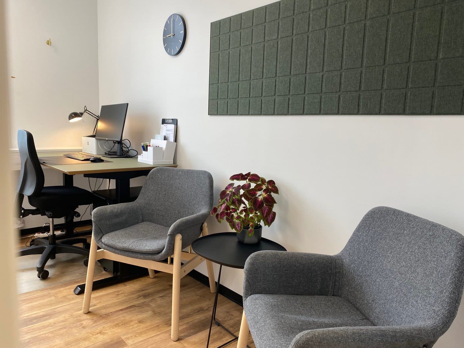 Konsultationsrum hos Privat Psykiatrisk Center Aalborg med arbejdsstation, grå lænestole og grøn akustikpanel