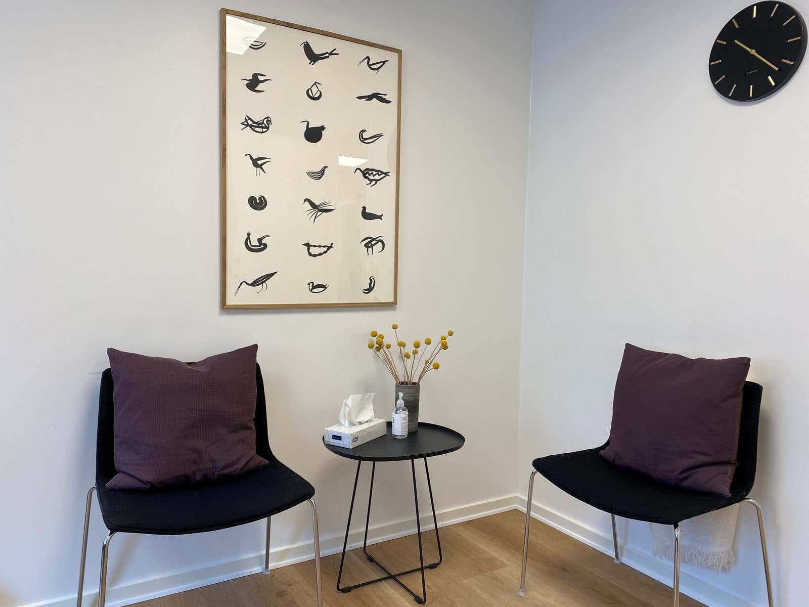 Lyst samtalerum med to stole, blomsterbuket og fugleplakat hos Privat Psykiatrisk Center Kolding