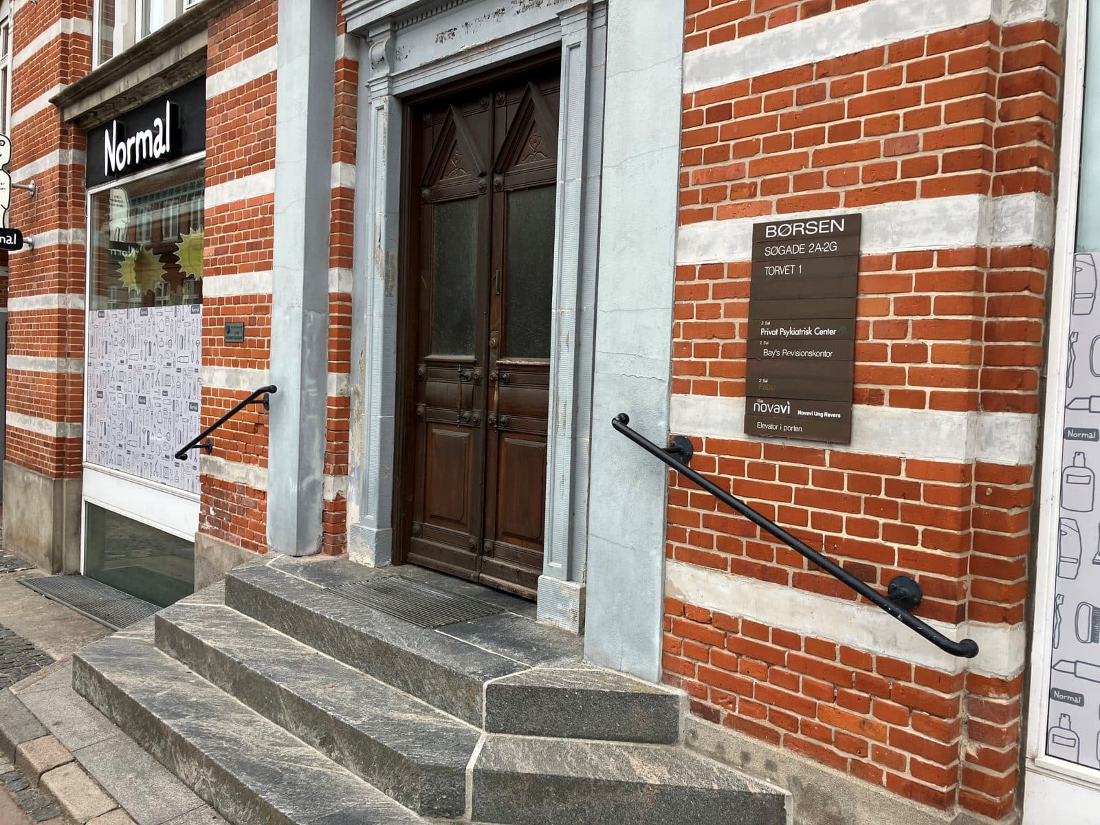 Hovedindgang til Privat Psykiatrisk Center Ringsted ved Torvet — rød murstensbygning med trappe og skiltning ved siden af butikken Normal